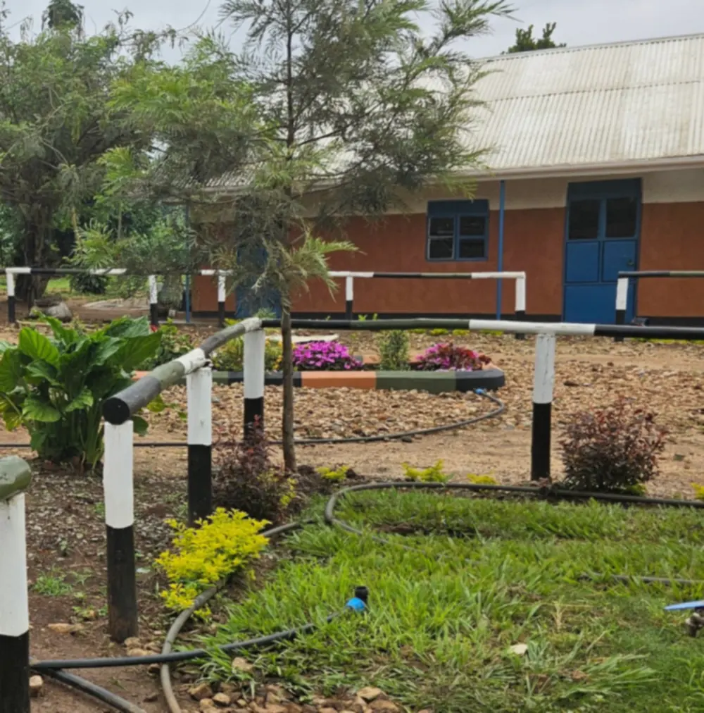 A classroom block with an orange wall and blue doors behind a fenced flower bed on the Spectrum Secondary School grounds.