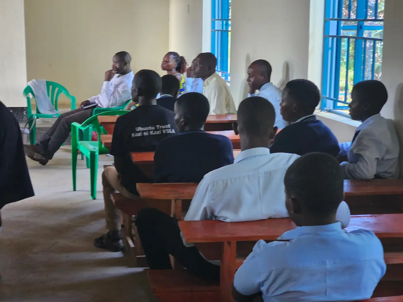 Learners, staff and community members seated on benches and chairs at a meeting in a classroom.