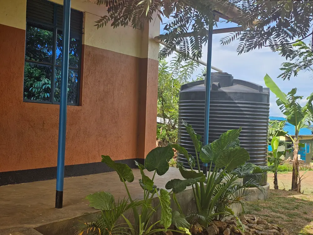 A large black rainwater tank beside a classroom block, fed by a pipe from the roof.