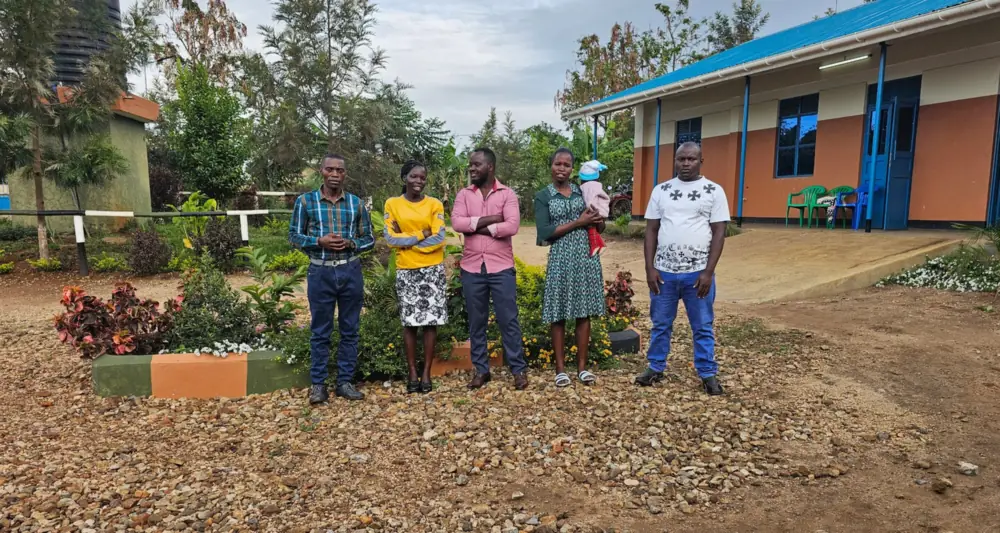 Five members of the Spectrum Secondary School team stand together in the school compound, in front of a classroom block and flower beds.